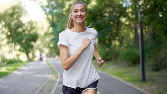 Woman in sports attire running on asphalt road.